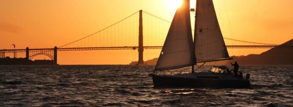 Sailboat silhouetted against a vivid orange sunset at the Golden Gate Bridge