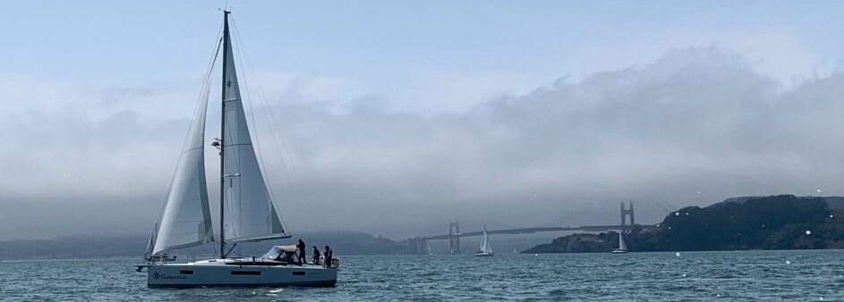 Tall ship and sailboat silhouetted under the Golden Gate Bridge at dusk